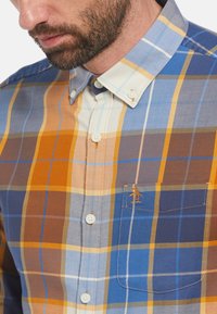 Katoenen geruite shirt met een mix van blauw, oranje en roomkleuren. Knop-down kraag, afgeronde borstzak met logo en witte knopen.