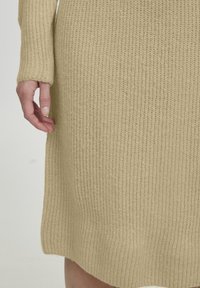 Gebreide jurk in lichtbeige, met ribbelstructuur, lange mouwen en een rechte snit met een kleine split aan de zoom.