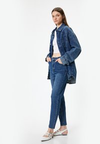 Veste en denim et jeans de ton bleu délavé, avec une coupe classique et un léger effet usé. Des chaussures blanches à lanières complètent le look.