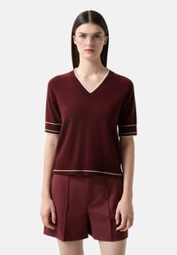 Bordový svetr s krátkým rukávem a výstřihem do V, s kontrastním krémovým lemem na rukávech a spodním lemu, spárovaný s odpovídajícími šortkami. Měkká pletená textura.