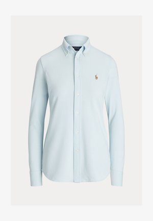 Gai zils krekls ar klasisko apkakli, garām piedurknēm un mazu izšūtu logotipu kreisajā krūšu pusē. Kokvilnas materiāls, gluda tekstūra.