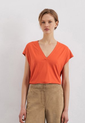 Short-sleeve orange T-shirt with a V-neck and relaxed fit, made of soft fabric, paired with light tan, high-waisted suede pants.