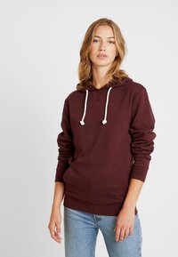 Bordeaux hoodie met een voorkantzak, witte trekkoordjes en geribbelde boorden. Zacht materiaal met een ontspannen pasvorm en capuchon voor casual draag. 