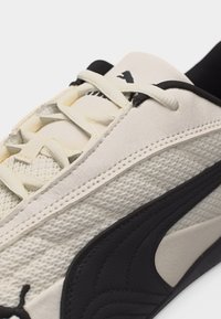 Gros plan sur une basket Puma blanche et noire montrant les lacets, la texture en mesh et le logo Puma sur la languette et le côté.