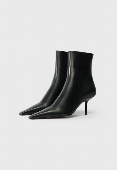 Botines de cuero negro con punta afilada, silueta esbelta y tacón de aguja. Textura suave y diseño minimalista.