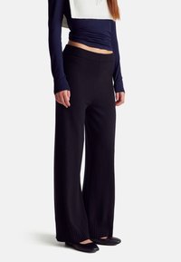 Černé kalhoty s širokými nohavicemi vyrobené z měkké tkaniny, s žebrovaným pasem a manžetami. Nosit s přiléhavým topem s dlouhým rukávem a plochými botami.