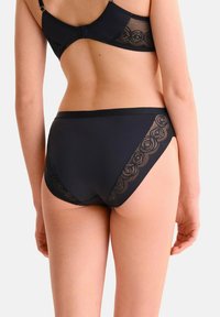 Ensemble de lingerie noire comprenant un soutien-gorge avec des accents en dentelle transparente et une culotte taille haute assortie avec des détails floraux en dentelle sur les côtés.