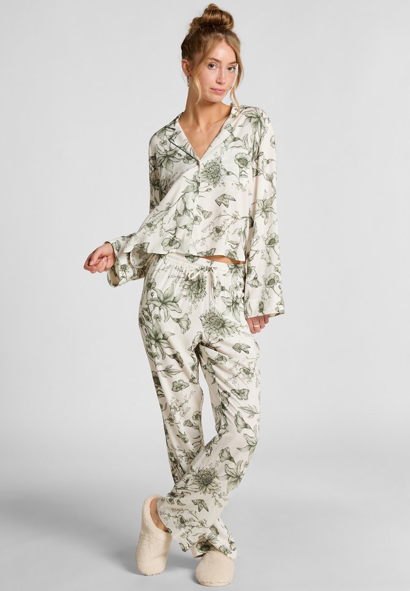 Bloemen pyjama set met een langmouwen top en broek met elastische taille in crème met groene botanische patronen. Zachte, lichte stof en een comfortabele pasvorm.