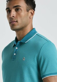 Polo shirt teal avec un motif texturé à carreaux. Avec un col contrastant et un petit logo sur la poitrine. Patte de boutonnage à trois boutons.