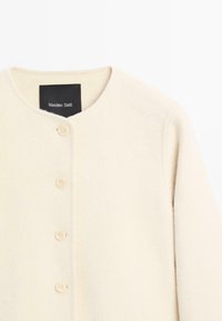 Cardigan di lana color crema con scollo rotondo, chiusura frontale con bottoni e quattro bottoni color crema, etichetta Massimo Dutti all'interno del colletto.