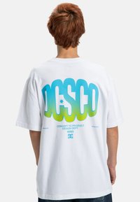 Weißes Baumwoll-T-Shirt mit einem großen blauen und grünen grafischen Text auf der Rückseite mit "DC" und "CONCEPT TO PRODUCT DESIGN DEPT."