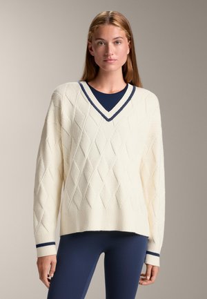 Cream-colored v-neck sweater featuring a textured diamond pattern, ribbed hem and cuffs, and navy blue accents. Long sleeves, relaxed fit.