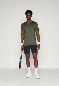 Grønn shortsleeve treningsskjorte med logo på ermet, kombinert med svarte shorts. Hvite håndleddbånd, hvite sko og et tennisracket med blå striper.