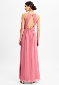 Roze maxi-jurk met een kanten rug, een vloeiende structuur en een aansluitende taille. Voorzien van spaghettibandjes en een lage rugopening.
