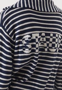 Marineblauwe en witte gestreepte gebreide trui met een groot, textuurgegeven "STAU"-logo op de achterkant. De kraag is omgeslagen met knoopaccenten.