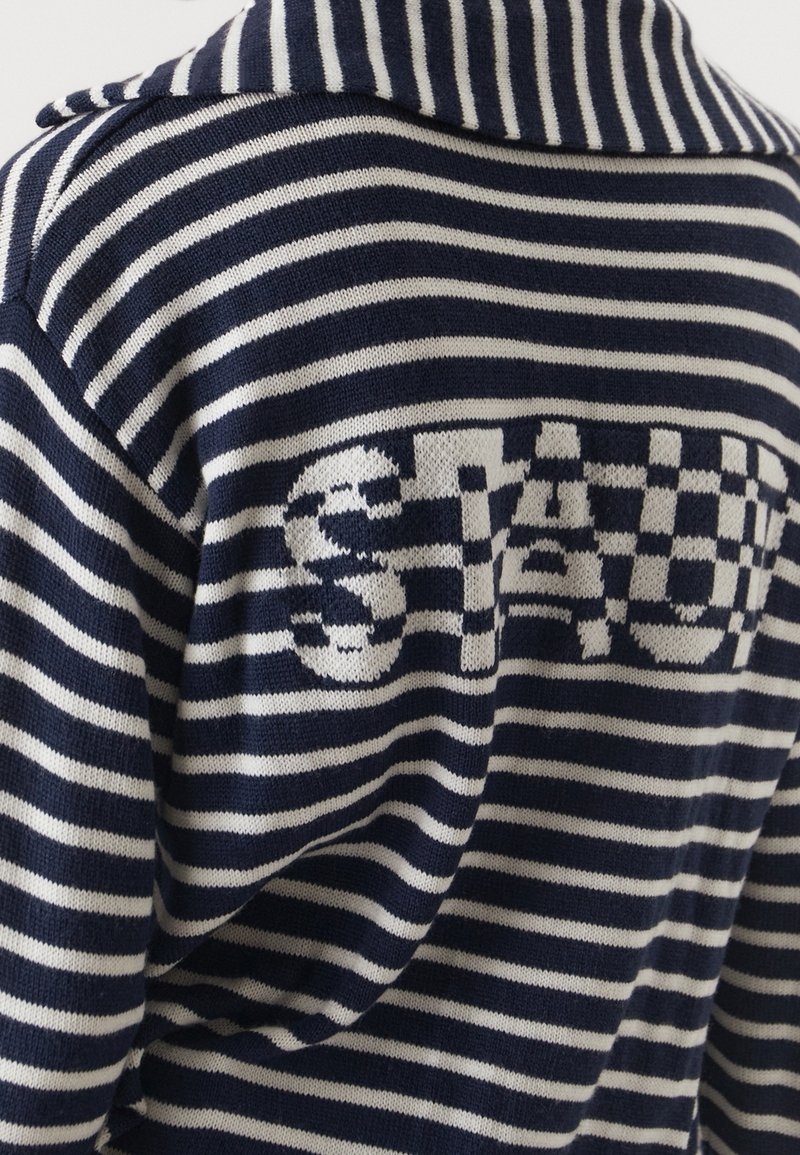 Marineblauwe en witte gestreepte gebreide trui met een groot, textuurgegeven "STAU"-logo op de achterkant. De kraag is omgeslagen met knoopaccenten.