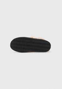 Zwarte rubberen zool van een slipper met een gestructureerd zigzagpatroon; zachte, pluche bovenkant in een lichtbeige kleur, ontworpen voor comfort.