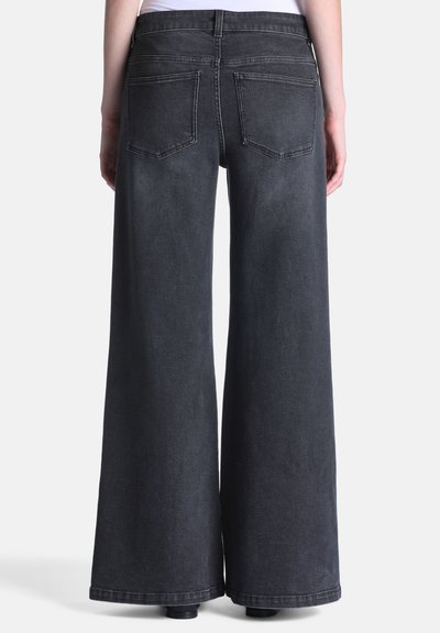 Jean en denim noir à jambes larges vu de dos avec deux poches arrière et une taille haute, porté avec un haut blanc.