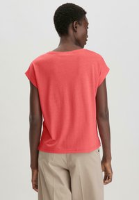 Koraalkleurig t-shirt met korte mouwen, ontspannen pasvorm, zachte stof, ronde halslijn en achterste naaddetails, gecombineerd met beige wijde broek.