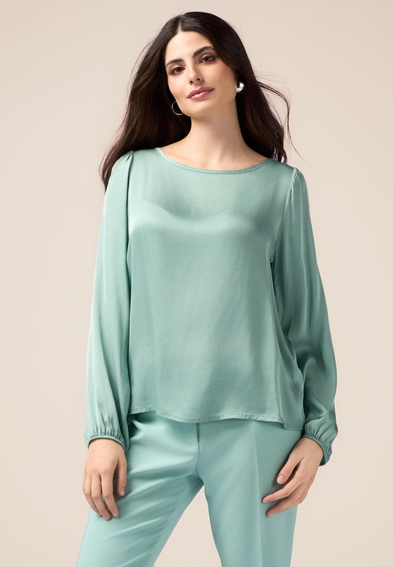 Blusa azzurro chiaro con maniche lunghe e vestibilità ampia. Tessuto morbido e leggero con scollatura rotonda e polsini arricciati. Abbinata a pantaloni coordinati.