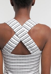 Achteraanzicht van een persoon in een mouwloos topje met brede, witte banden die in een X-vorm gekruist zijn en zwarte horizontale strepen.