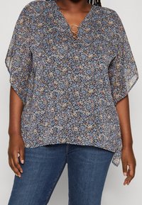 Blusa floreale in tessuto trasparente con sfondo blu navy. Caratterizzata da scollatura a V, hardware circolare dorato e maniche ampie a pipistrello.