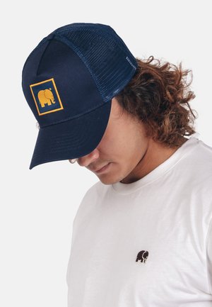Marine baseballpet met een gaasachterkant, voorzien van een geel olifantenlogo op het voorpaneel. Draagt een wit T-shirt met een klein logo.