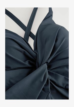 Ciemnoniebieski top kąpielowy z wykręconym wzorem na środku, wykonany z gładkiego materiału. Posiada podwójne, wąskie ramiączka krzyżujące się na plecach.