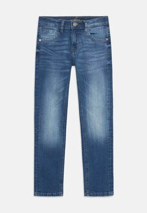 Jeans aderenti blu slavati con tasche anteriori, passanti per cintura e chiusura con bottone del marchio Guess su uno sfondo neutro.