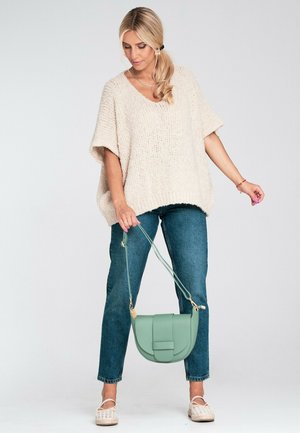 Beżowy, oversize'owy sweter z krótkimi rękawami, zestawiony z niebieskimi dżinsami i jasnozieloną torebką na ramię. Stylizację dopełniają espadryle.