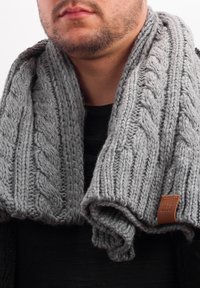 Gray knitted scarf with a cable pattern, soft texture, and a leather tag. Worn loosely around the neck.