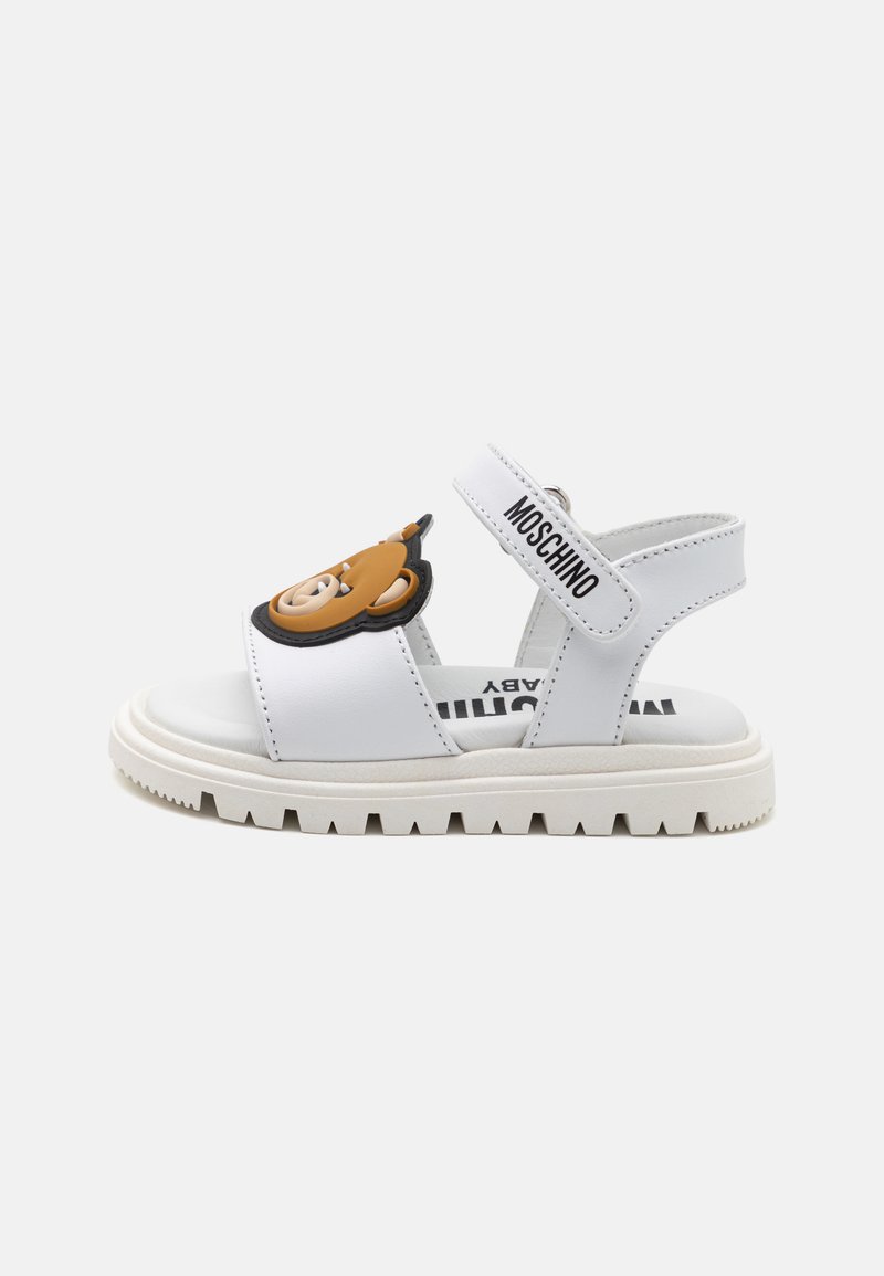 Sandali bianchi con una fascia imbottita che presenta un adorabile design di orsetto, chiusura in velcro e una suola spessa bianca. Il marchio è visibile sulla fascia.