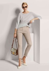 Hellgrauer Strickpullover, beigefarbene, cropped Hose mit ausgefranstem Saum, weiße Slingback-Absätze und eine kleine braun-creamfarbene Handtasche.
