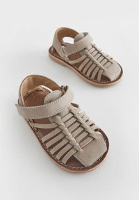 Beige mockasksandaler med öppen design, med korsade remmar, justerbar ankelsnodd och sydda detaljer på sulan.
