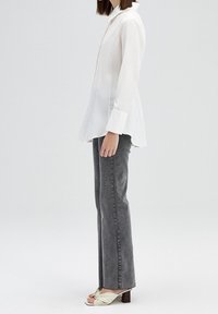 Witte lange mouwen shirt met een puntige kraag en een A-lijn silhouet, gecombineerd met grijze rechte jeans en lichtgekleurde hakken.