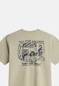 Camiseta de algodón beige con un estampado gráfico de un camión de entrega y el texto: "EN RUTA DE ENTREGA" en azul marino. Mangas cortas, ajuste estándar.