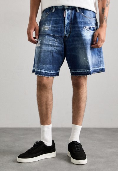 Denim shorts in light to dark blue with distressed details and frayed hem. Paired with black sneakers and white socks.