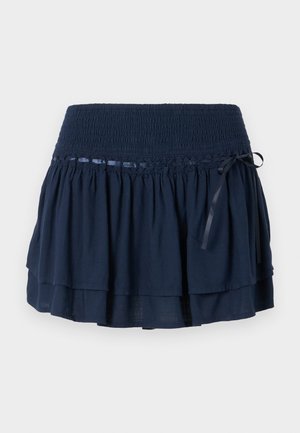 Mørkeblå nederdel med smocket talje, lagdelt voluminøst design, satinbånddetalje og diskret dekorativ syning.