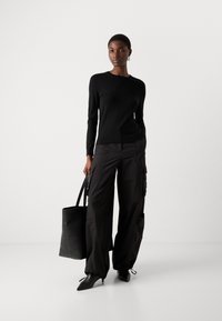 Μαύρο πουλόβερ με μακριά μανίκια συνδυασμένο με χαλαρές μαύρες cargo παντελόνες, κρατώντας μια μαύρη τσάντα ώμου. Διαθέτει μυτερές γόβες και διακριτή υφή στο ύφασμα.