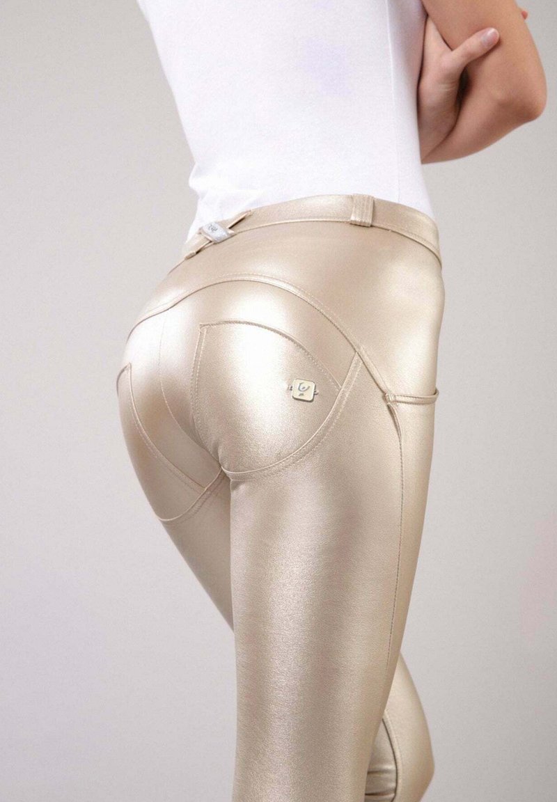 Leggings dorati lucidi con un design elegante, dotati di tasche posteriori e un piccolo logo in metallo vicino all'orlo della vita. Texture liscia e aderente.