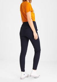 Pantalones ajustados de color azul marino, elásticos, con cinturilla elástica y bolsillos laterales, combinados con una camiseta de manga corta naranja y zapatillas blancas.