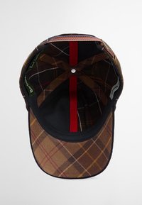 Καφέ καπέλο με καρό σχέδιο που διαθέτει μαλακή υφασμάτινη επιφάνεια, μαύρη πλευρά κάτω από το γείσο και κόκκινη κάθετη ρίγα στο εσωτερικό. Περιλαμβάνει ετικέτα λογότυπου.