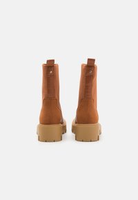 Bottes chevilles marron avec une finition en cuir lisse, des panneaux latéraux élastiques et des semelles en caoutchouc proéminentes ; elles sont dotées de tirettes à l'arrière pour un enfilage facile.