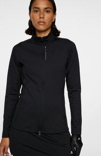 Sort zip-up jakke lavet af glat materiale med høj krave og lange ærmer. Inkluderer logo akcenter og en tætsiddende silhuet.