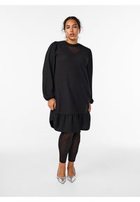 Čierne šaty s nafúknutými rukávmi a volánovým lemom, vrstvené cez čierne legíny s bodkami. Dokončené so striebornými špicatými podpätkami.