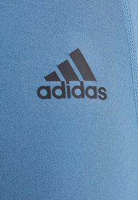 Blue athletic shirt made of textured fabric featuring a black Adidas logo on the front, with a smooth finish and a fitted design.