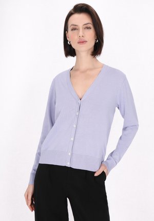 Cárdigan morado claro con escote en V, cierre frontal de botones, puños y dobladillo acanalados, y una textura suave. Combinado con pantalones negros.