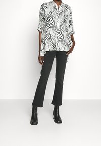 Svart och vit randig blus med hög-låg fåll, knäppning framtill, uppvikta ärmar; matchad med svarta utsvängda jeans och ankelboots.