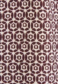 Tessuto di cotone con un motivo geometrico di forme rosso scuro su uno sfondo avorio, caratterizzato da disegni esagonali e ovali distribuiti uniformemente.
