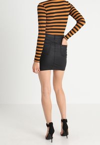 Randig långärmad topp i orange och svart, tillsammans med en åtsittande minikjol i svart konstläder med två bakfickor. Svarta klackskor.